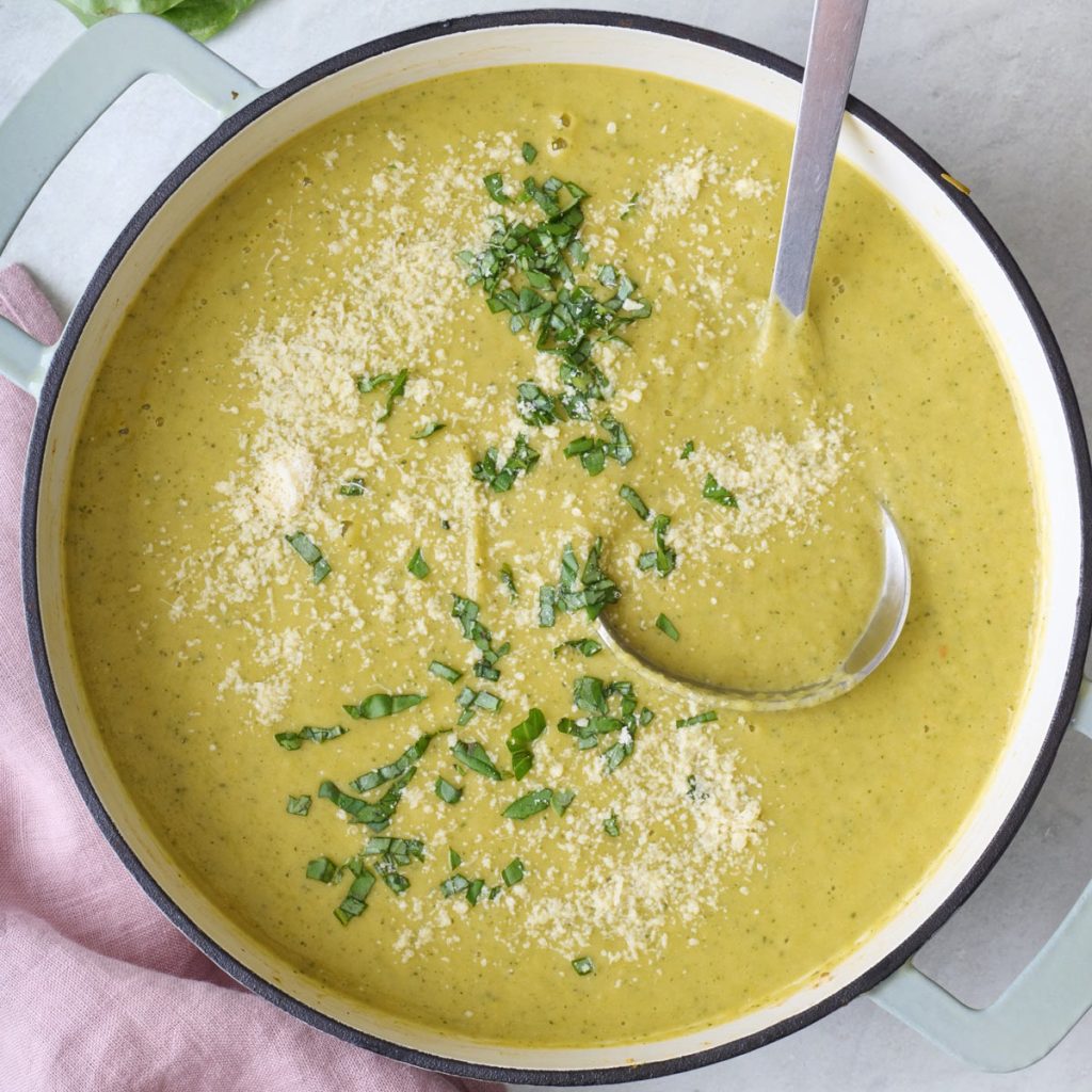 Creamy zucchini soup served in a white bowl, garnished with fresh parsley and a drizzle of olive oil, with a slice of crusty bread on the side.